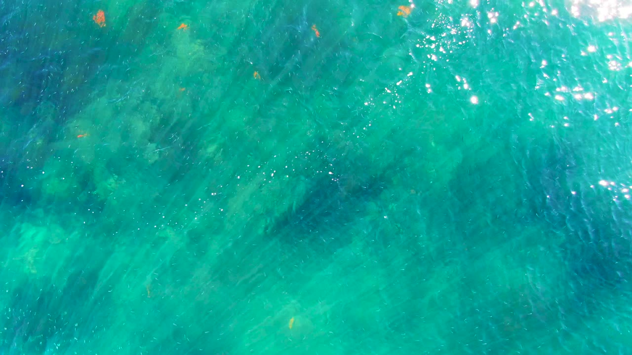 Clear turquoise water with glare and faint darker areas below the surface.