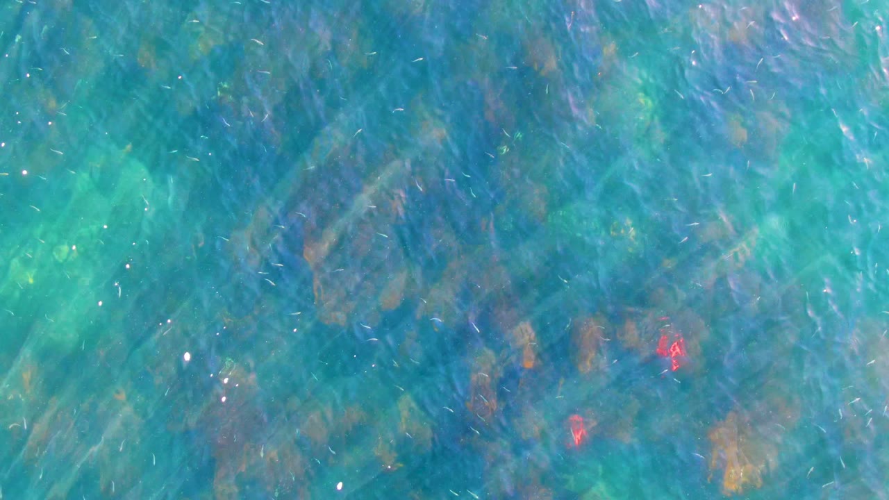 Clear turquoise water in La Bocana, Baja California Sur shows submerged rocks beneath bright ripples, with no visible people.