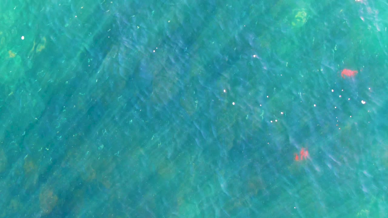 Clear turquoise shallows in La Bocana show rippled light, darker submerged rock or coral patches, scattered sun reflections, and no visible people.