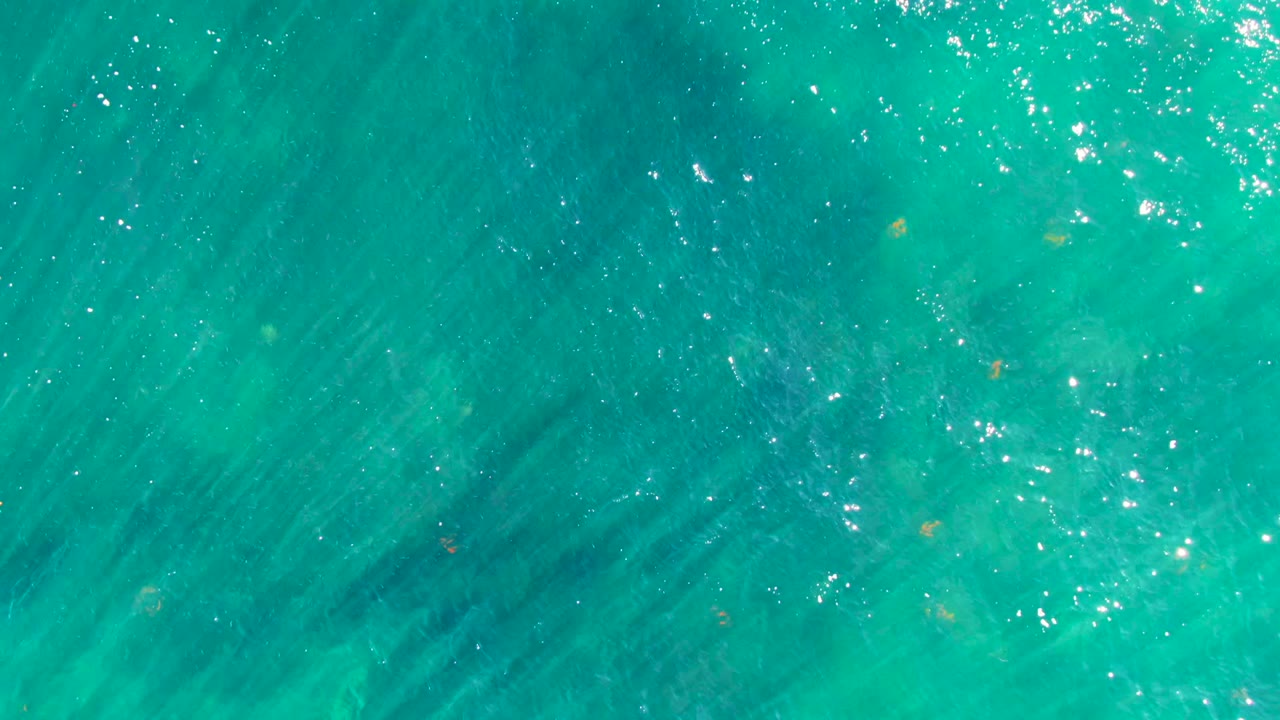 Clear turquoise water in La Bocana, Baja California Sur, with a bright cluster of reflected sunlight near the upper edge, darker underwater texture, and no visible people.