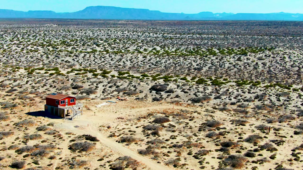 Red shack near center-left surrounded by desert shrubs.