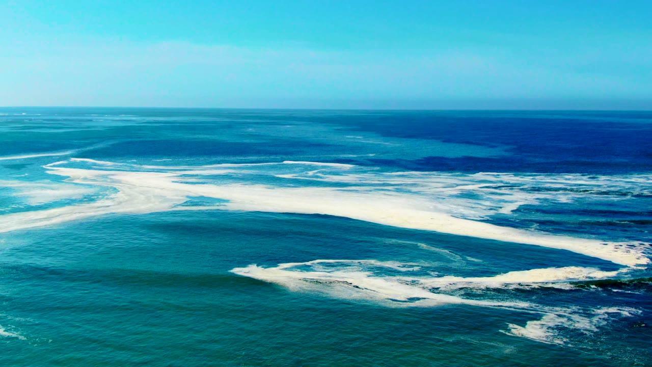 Wide ocean surface with curved white foam bands and blue water.