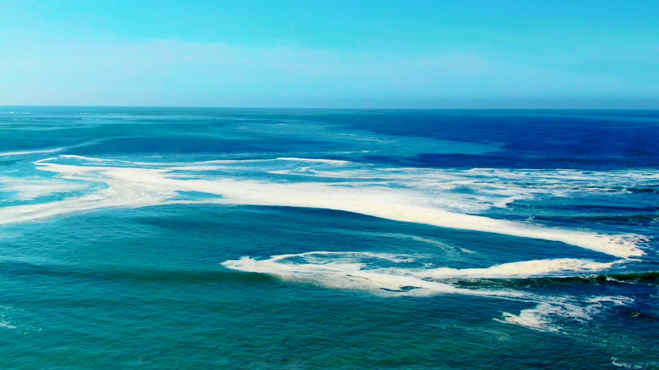 At 0:02, whitewater arcs stretch across the turquoise ocean at La Bocana, with darker blue water near the horizon and no visible people.