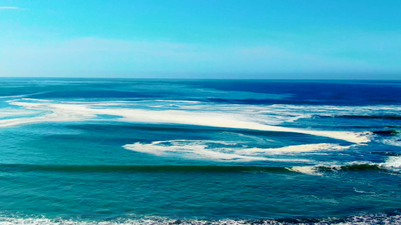 At La Bocana, Baja California Sur, turquoise ocean water stretches under a clear blue sky while white surf breaks across the midground, with no visible people.