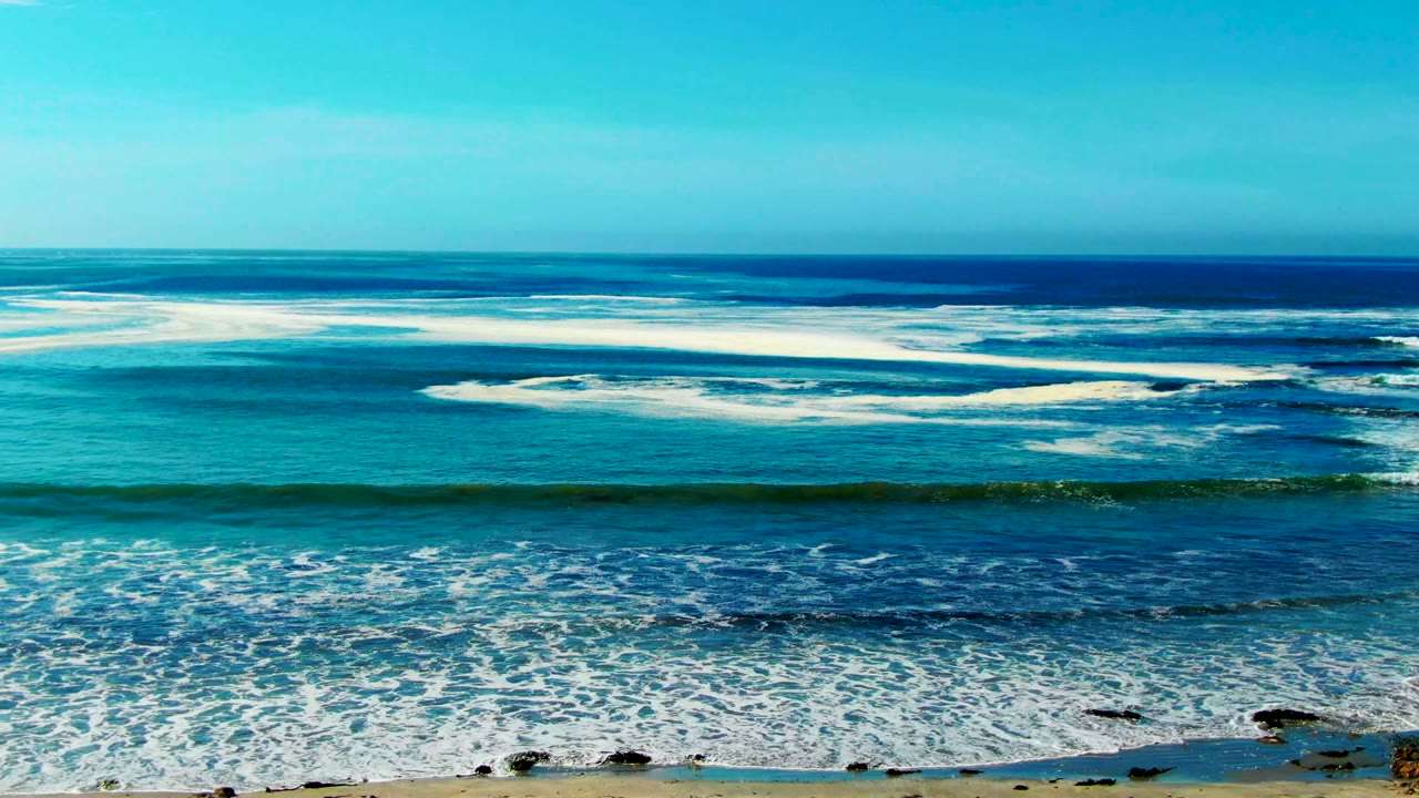 Breaking surf bands spread across turquoise water under a clear sky.