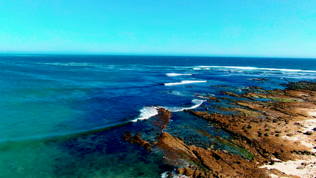 Rocky point extends into turquoise water as waves break offshore.