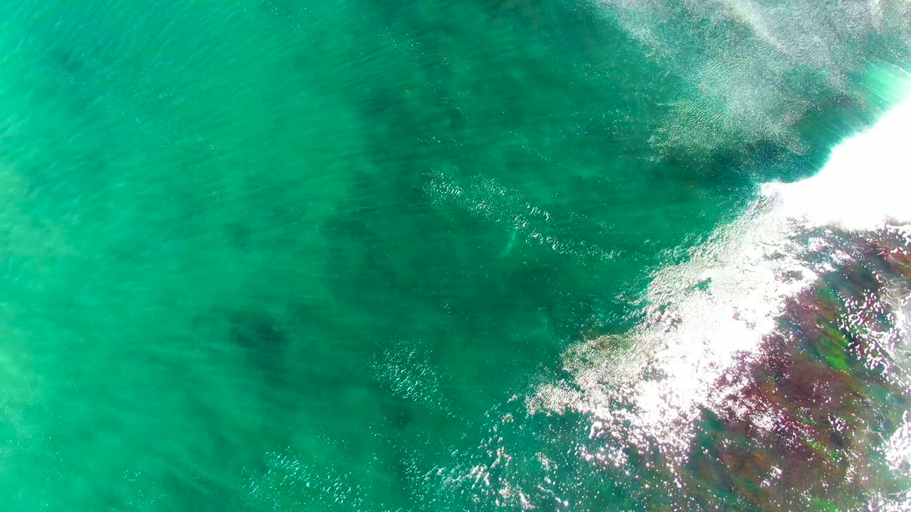 White wave foam spreading across turquoise water and submerged rocks