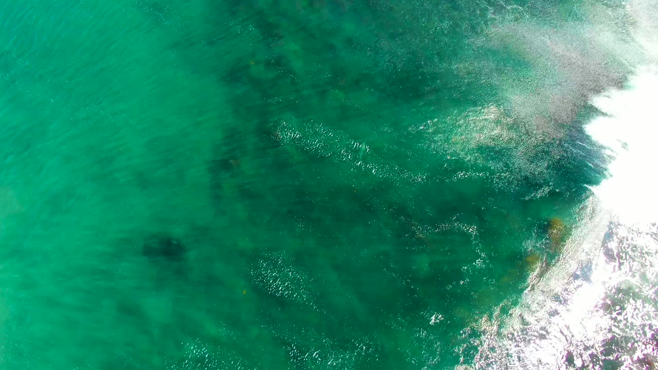 Top-down view at La Bocana, Mexico, showing a darker submerged rock field under turquoise water as bright surf breaks along the right edge, with no visible people.