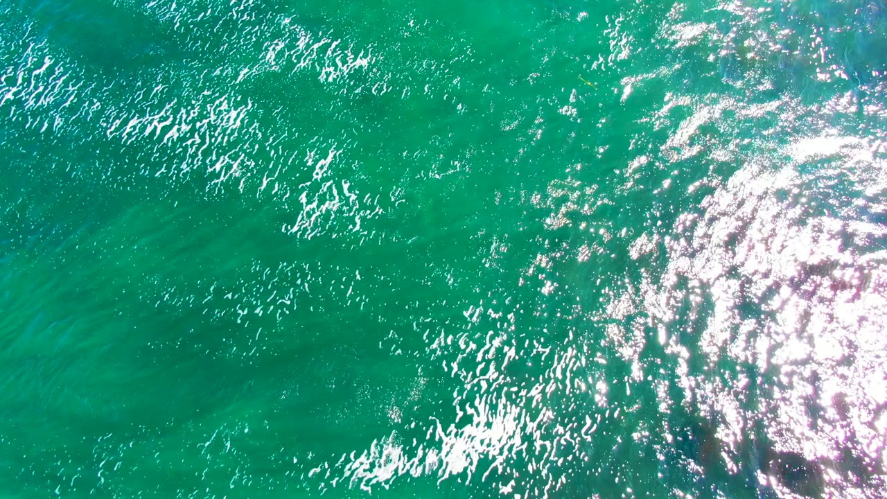 Clear turquoise sea surface with bright sunlight reflections.