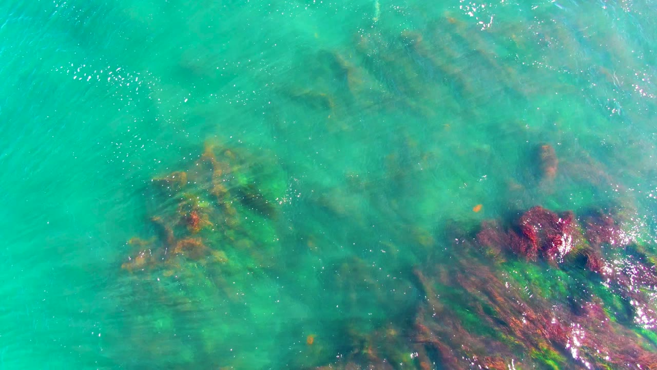 Clear green-blue water with submerged rocks and ripples.