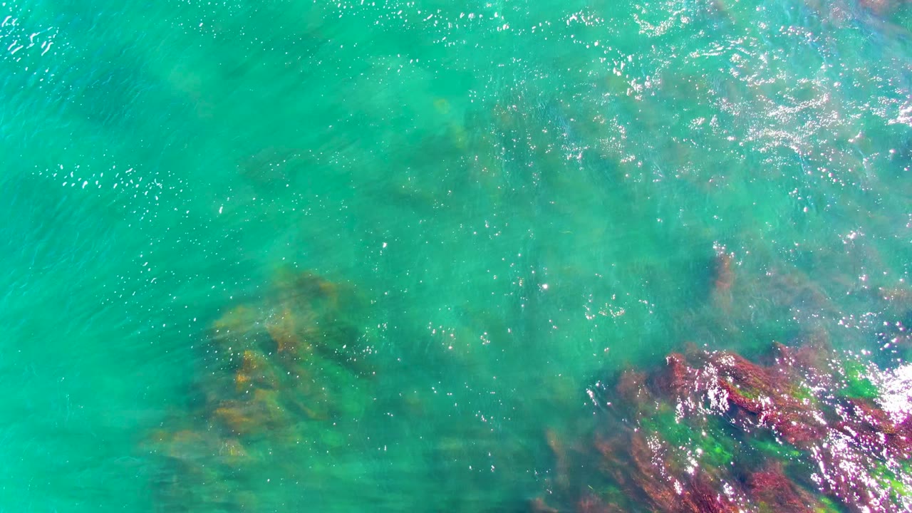 Overhead turquoise sea in La Bocana with submerged rock forms partly obscured by brighter surface glare and no visible people.
