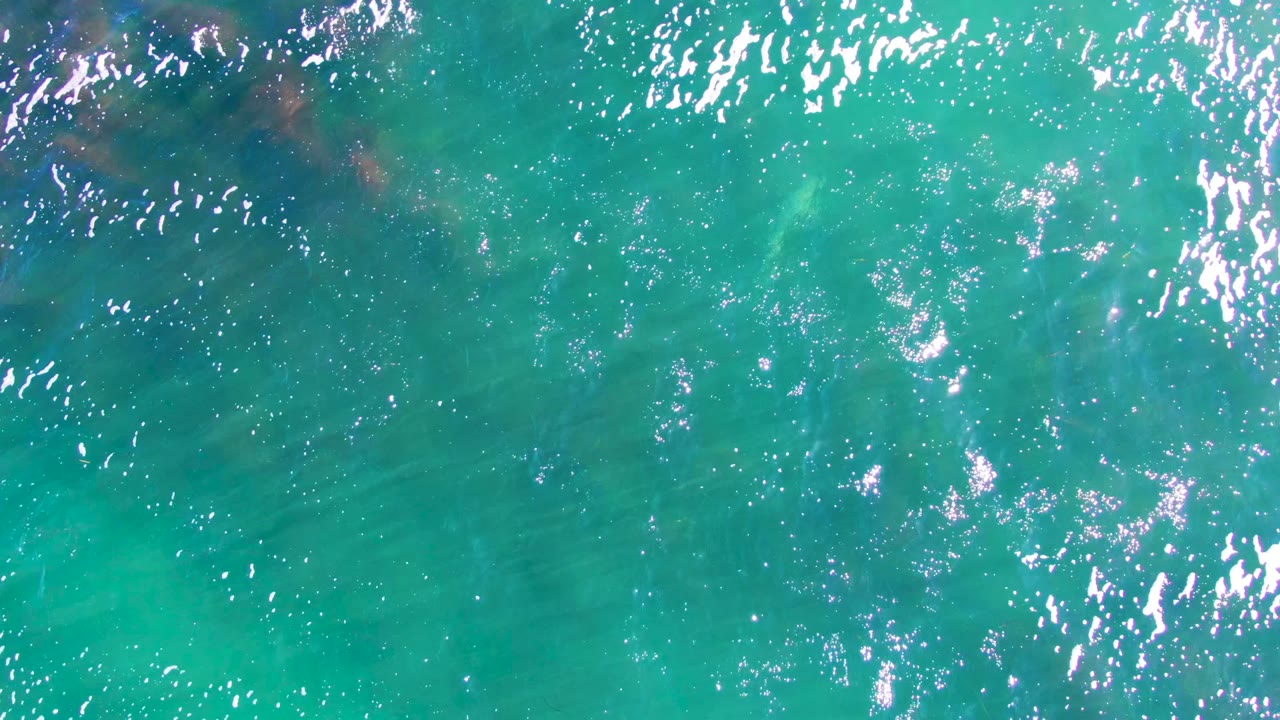 Overhead La Bocana water frame with bright ripples across turquoise water, a darker submerged shape near the upper area, and no visible people.