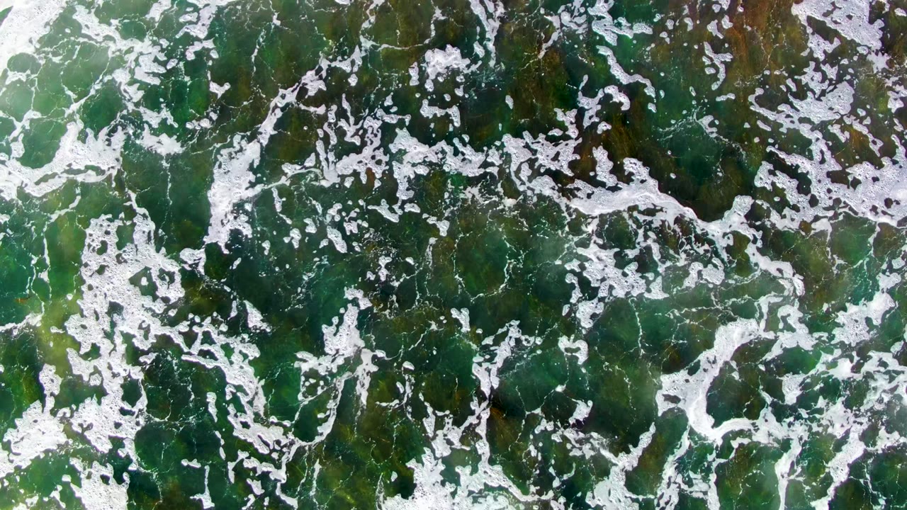 Overhead La Bocana view with broken white foam lines spread across green water and brown seaweed patches, no visible people.