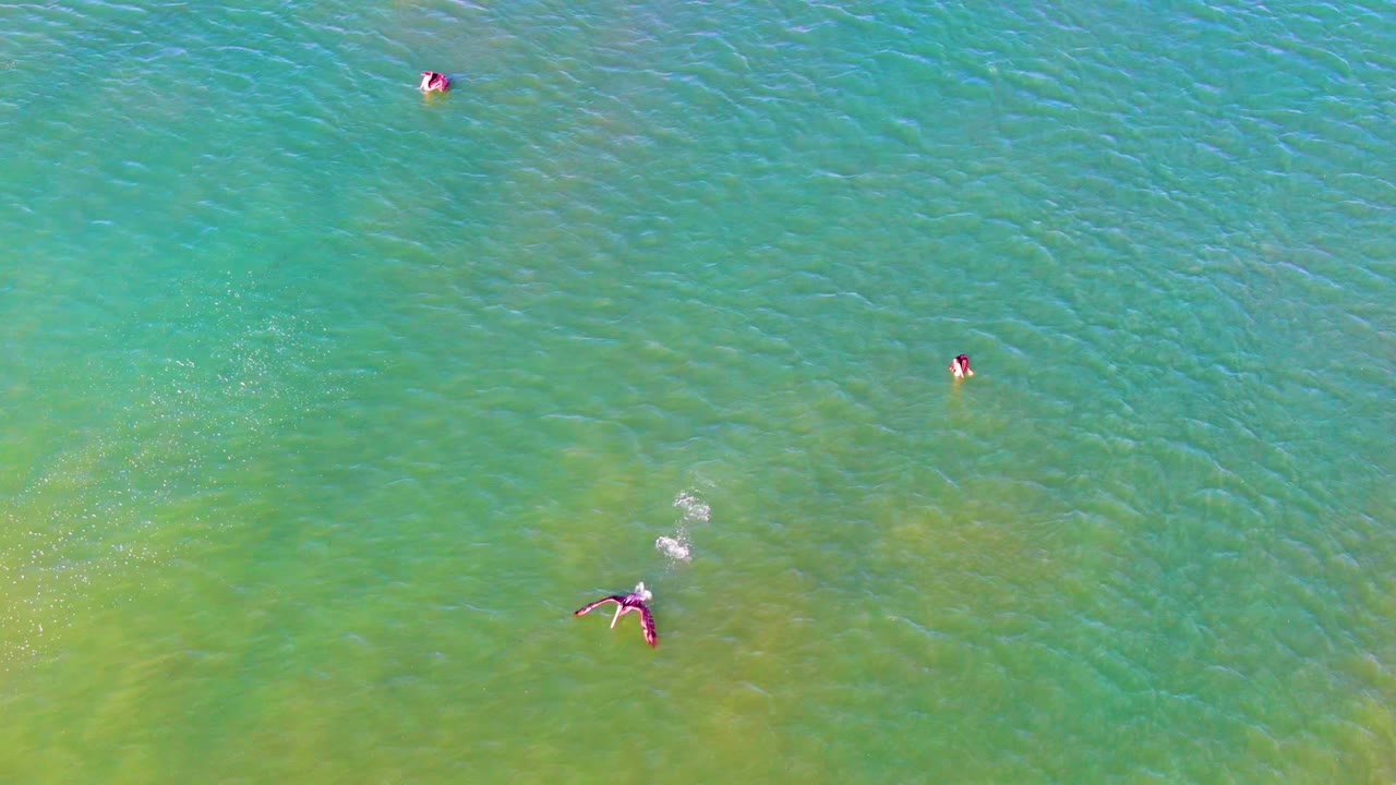Small swimmers spaced across rippled shallow ocean water.