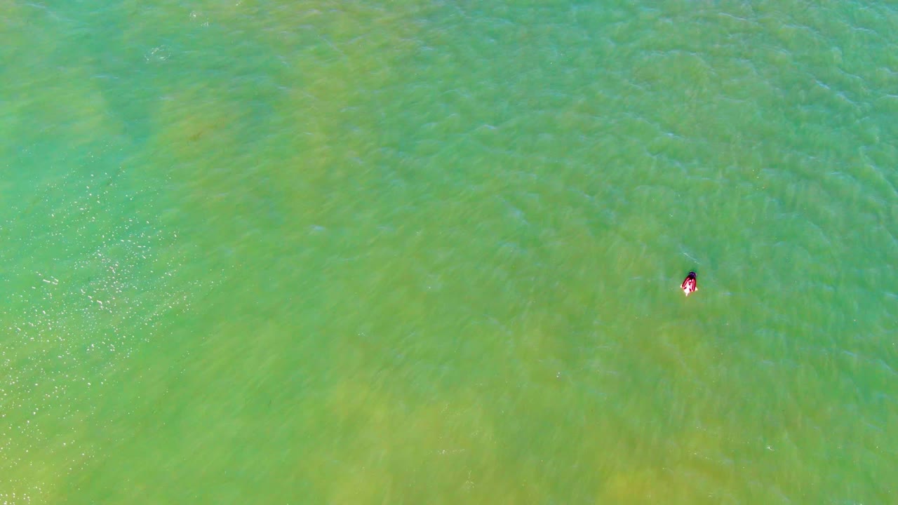 Overhead frame from La Bocana, Baja California Sur showing a small swimmer near the upper middle of clear green water with faint ripples around them.
