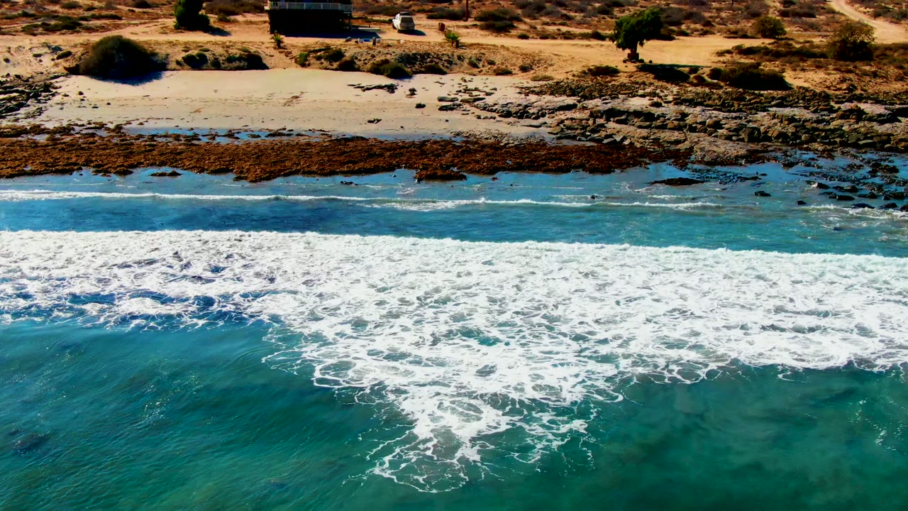 Foamy wave line breaking beside a sandy beach and rocky shelf