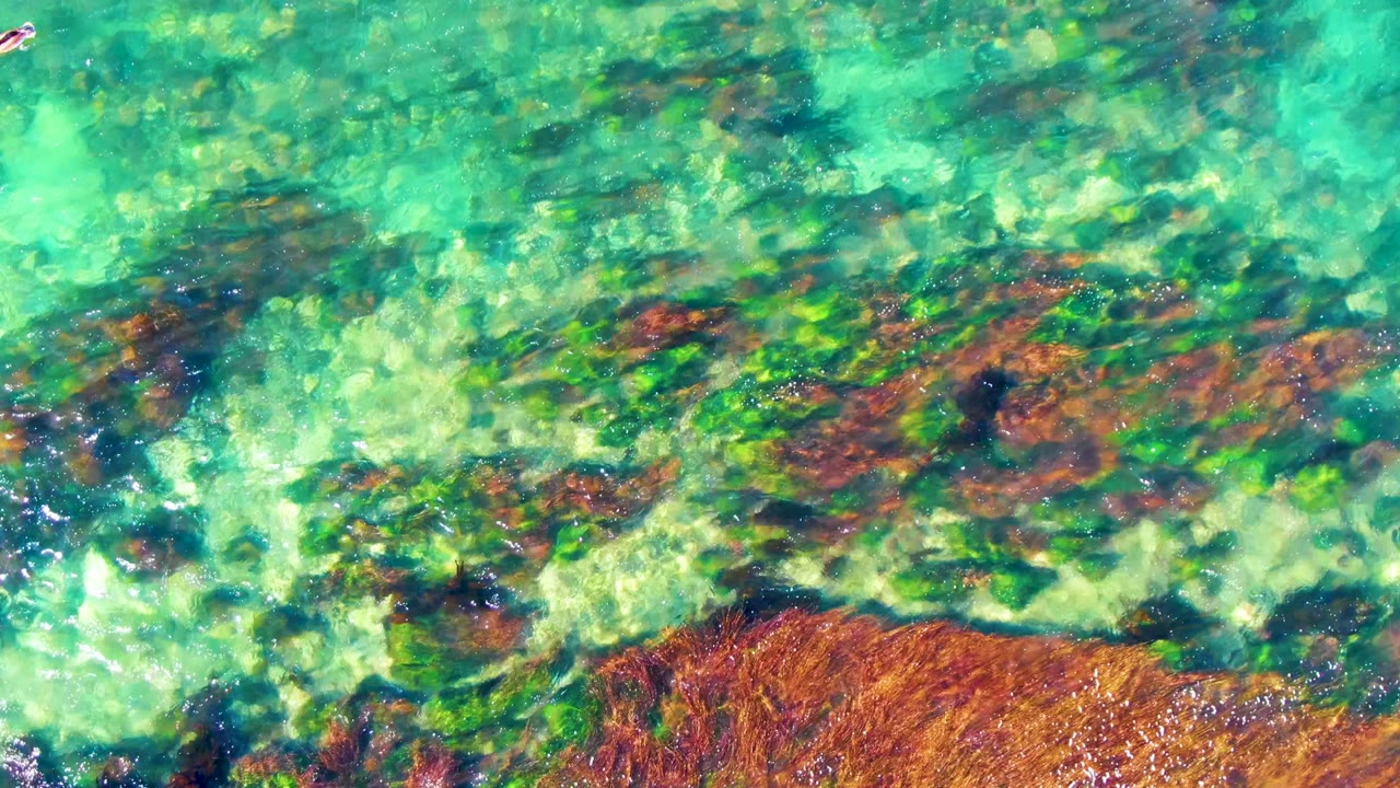 Ripples crossing clear water above brown rocks