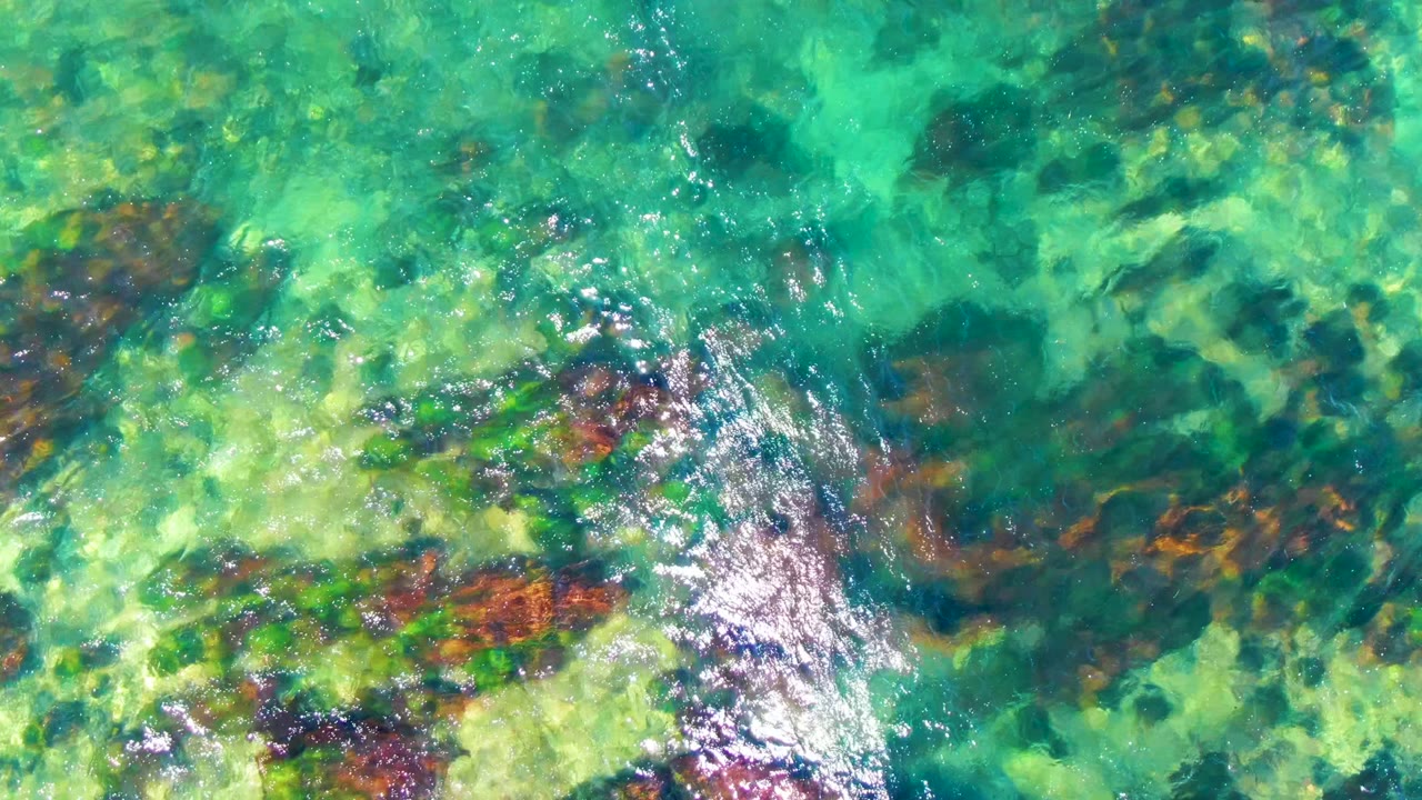 Clear green-blue water with rocks and bright ripple highlights.