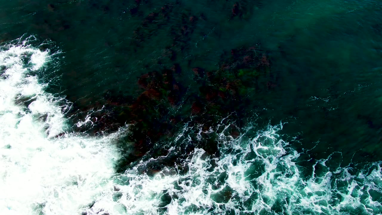 Breaking wave spreads across rocky ocean surface