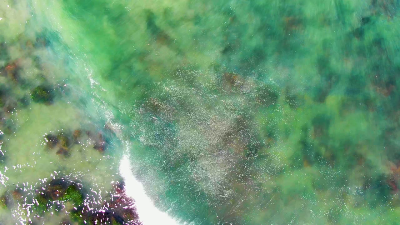 Clear green-blue ocean with reef patches and diagonal wave foam.