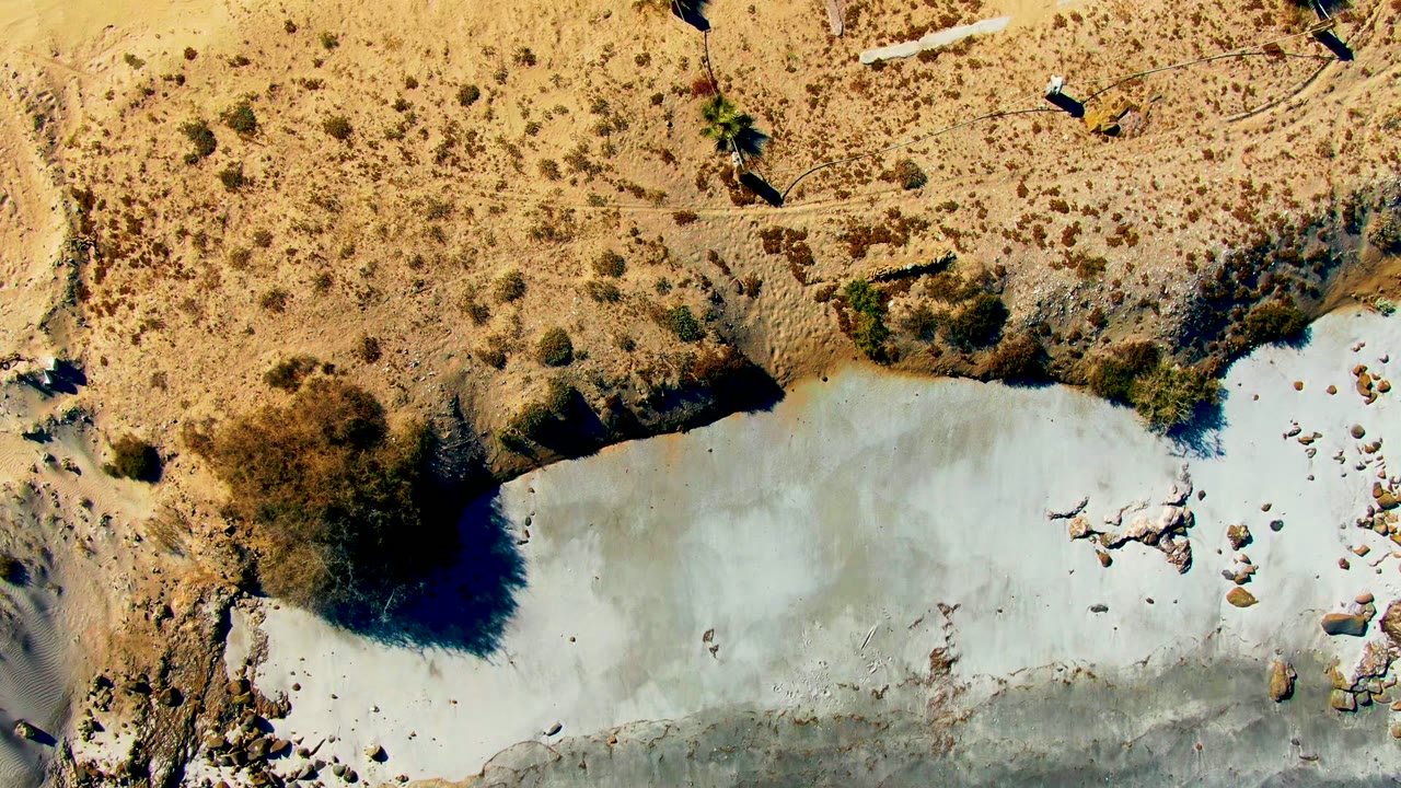 Overhead view of a pale pond edge surrounded by dry scrub and rocks.