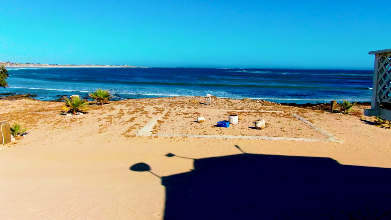 La Bocana beach view with a rectangular sandy area, small rocks and objects, a structure edge on the right, blue ocean beyond, and no visible people.