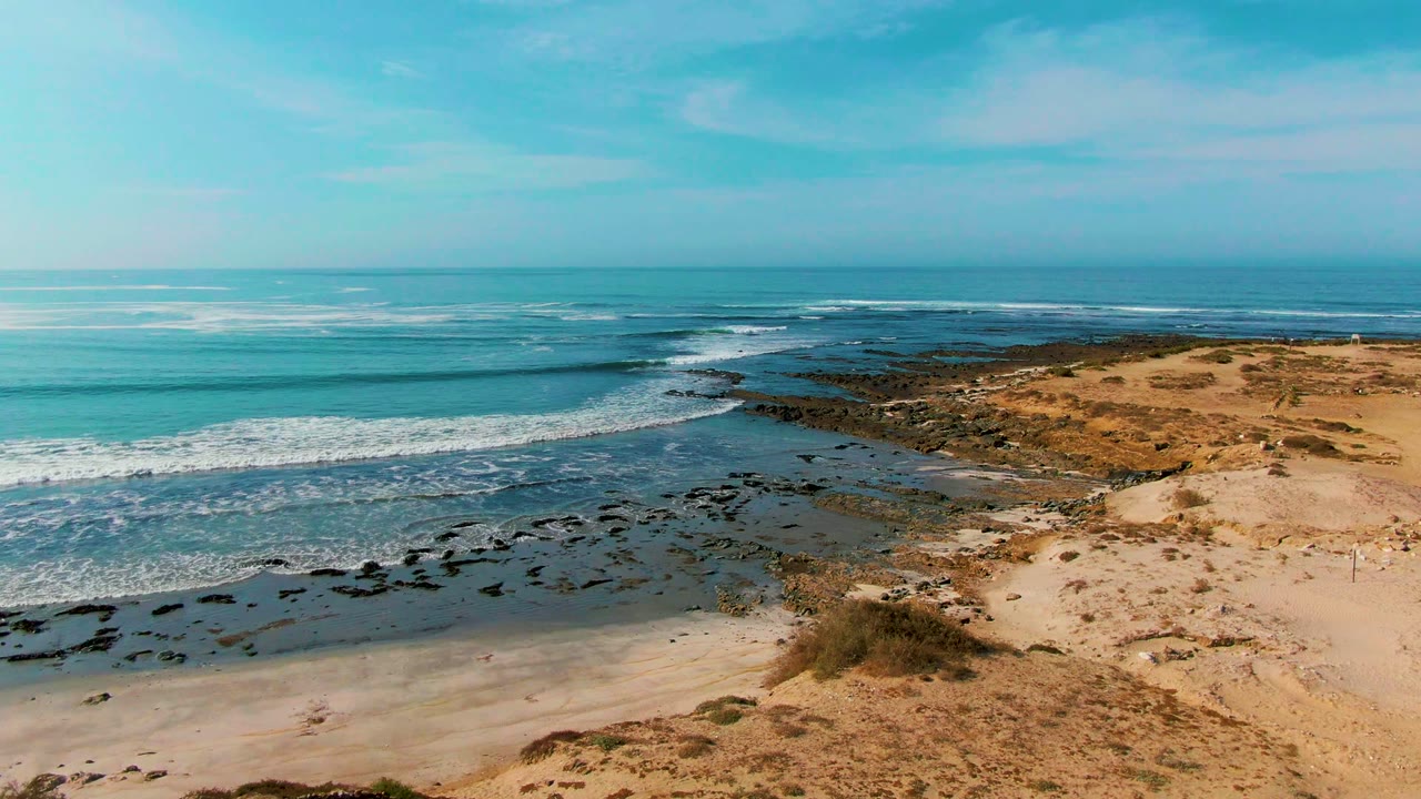 Waves roll toward dark rocks beside a sandy beach.