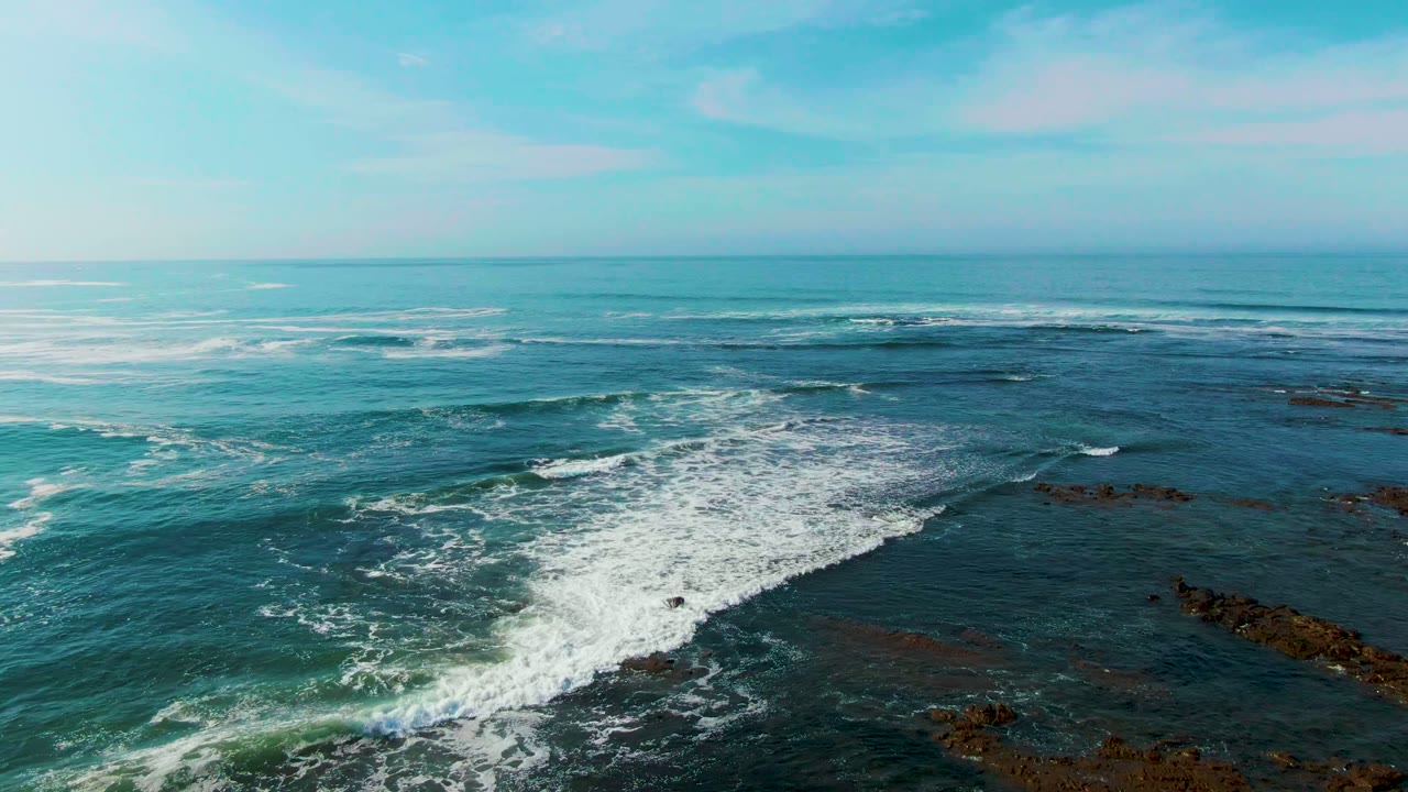 White wave line breaking across dark blue water and rocks.