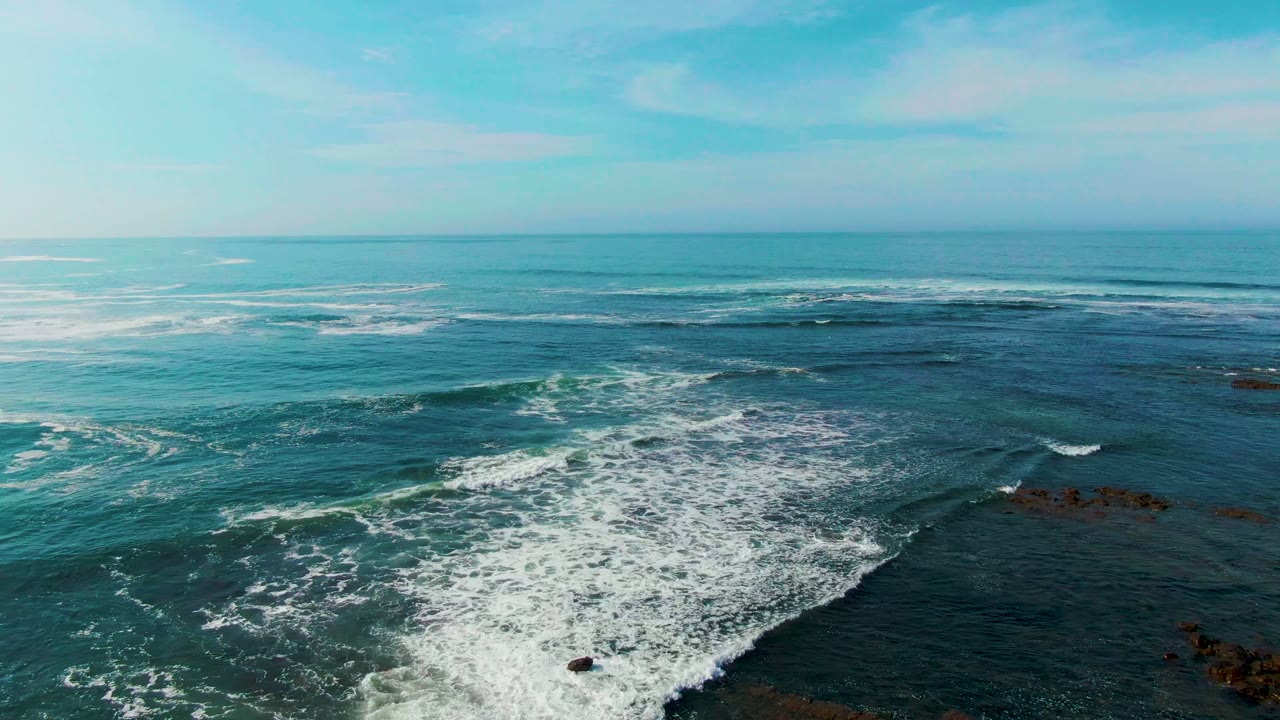 At 0:02, foamy surf expands across the center of the La Bocana ocean view, with scattered rocks to the right and no visible people.