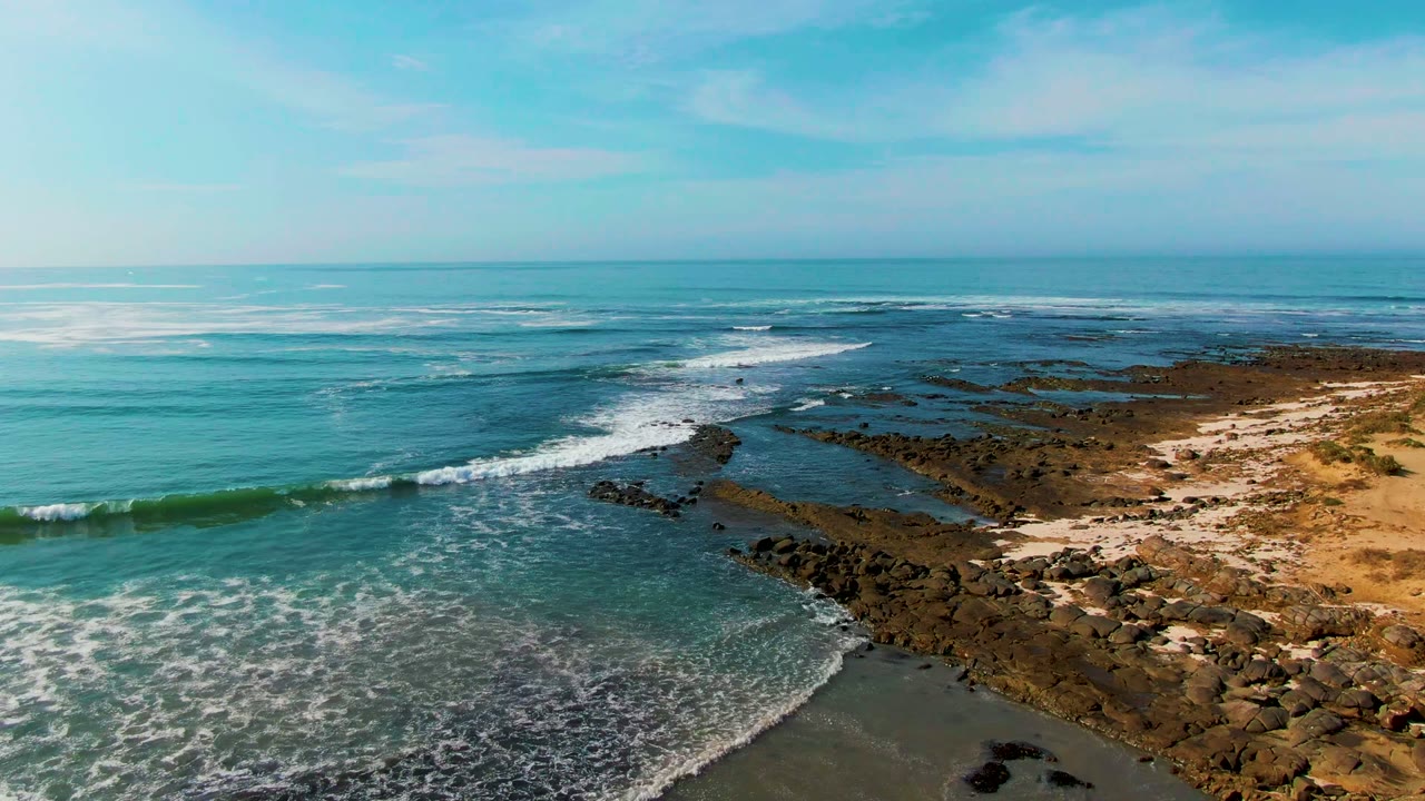 Aerial view of turquoise surf approaching the rocky and sandy La Bocana coastline in Baja California Sur, Mexico, with no visible people.