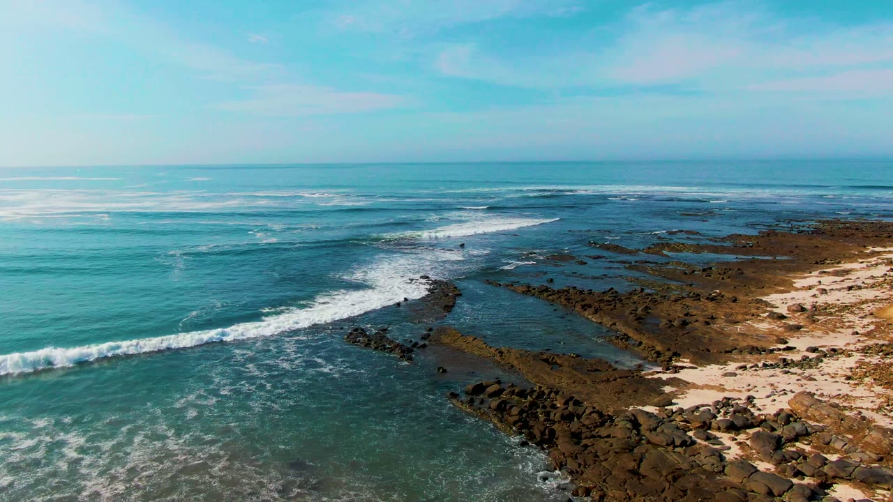 White surf line curling toward dark rocks and shallow reef