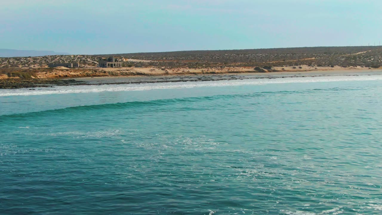 Low ocean swell moving toward a sandy beach and rocky shore.