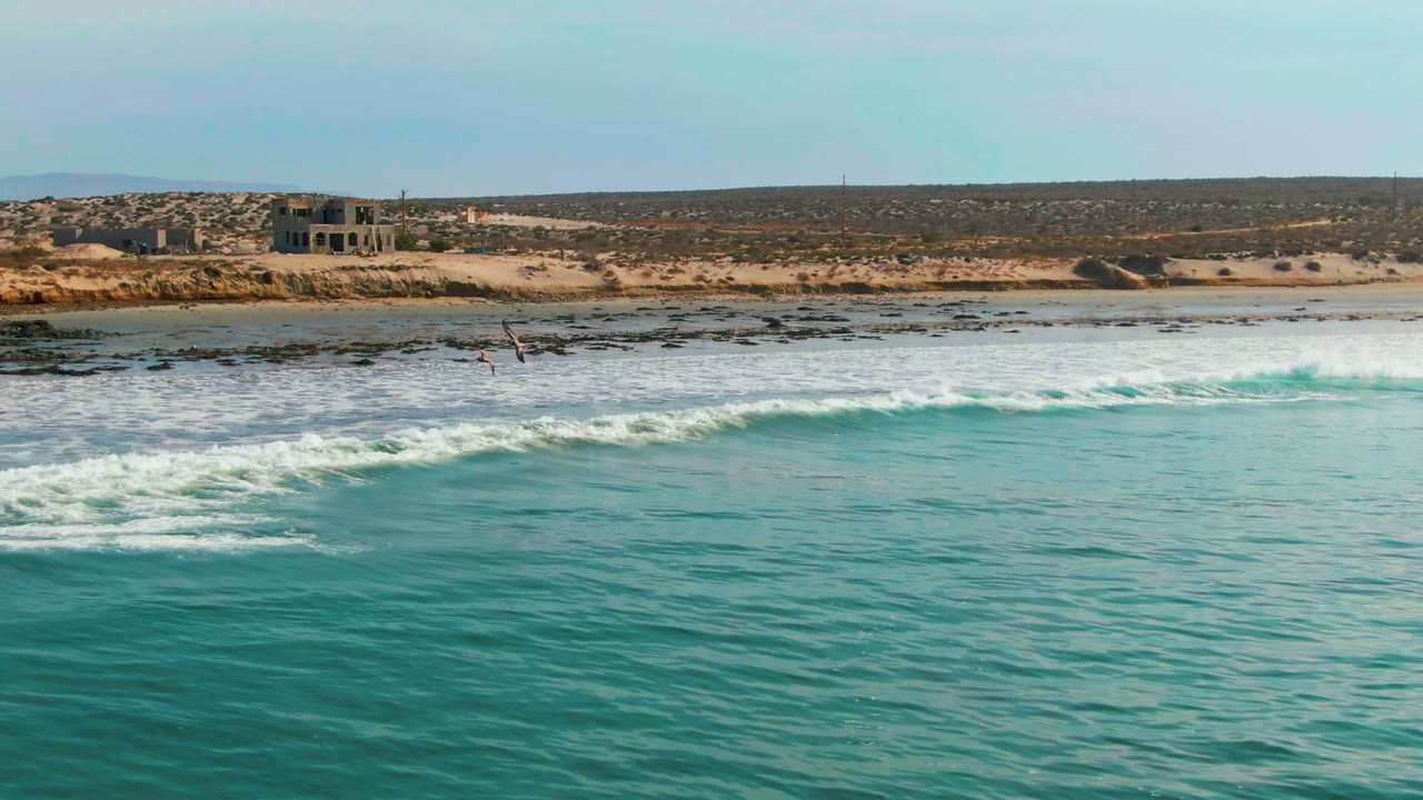 White surf spreads across turquoise water below a dry sandy shoreline.