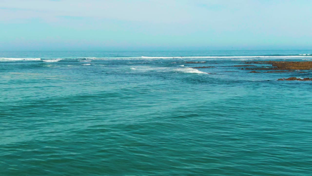 Open turquoise water with white waves breaking near dark rocks.