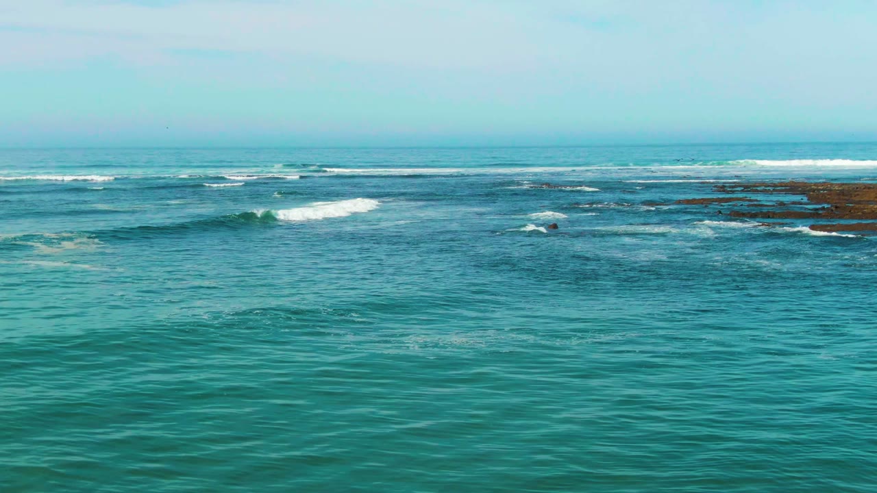 Wide view of turquoise ocean at La Bocana, Baja California Sur, with small whitecaps breaking near dark reef patches and no visible people.