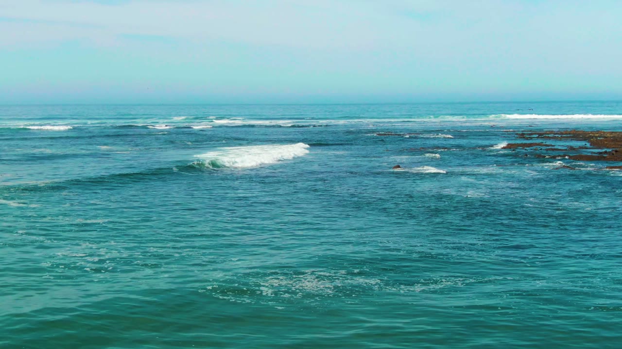 At 0:02, a brighter white wave crest breaks across turquoise water near the center of the La Bocana reef line, with no visible people.