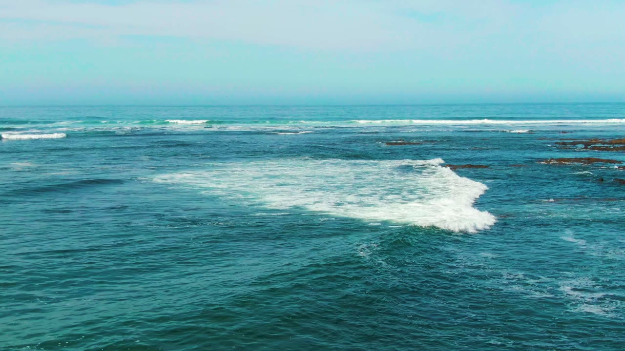 Ocean surf spreads into white foam over shallow rocky water.