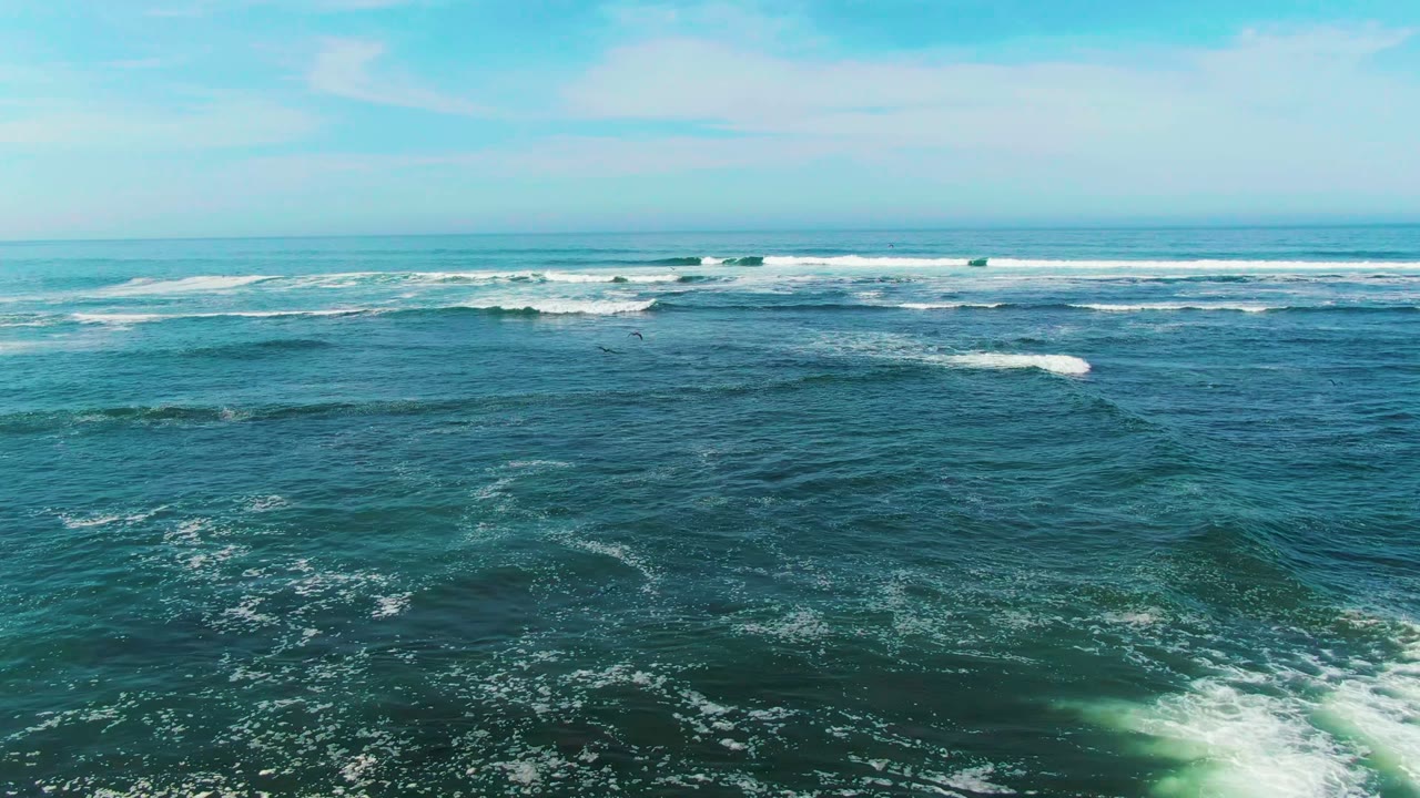 Wide aerial view over La Bocana ocean water with white surf bands near the horizon, darker teal foreground water, and no visible people.