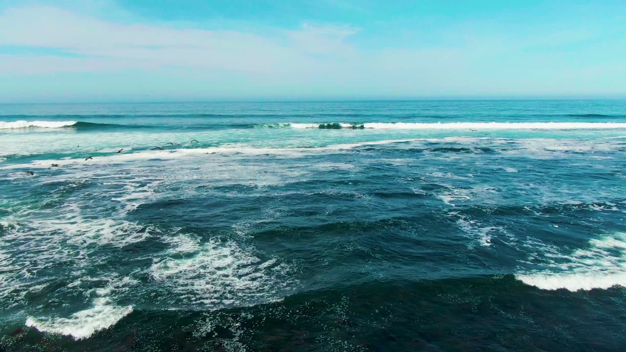 Wide view of La Bocana ocean water with dark blue foreground chop, white foam bands, distant breaking surf, scattered clouds, and no visible people.