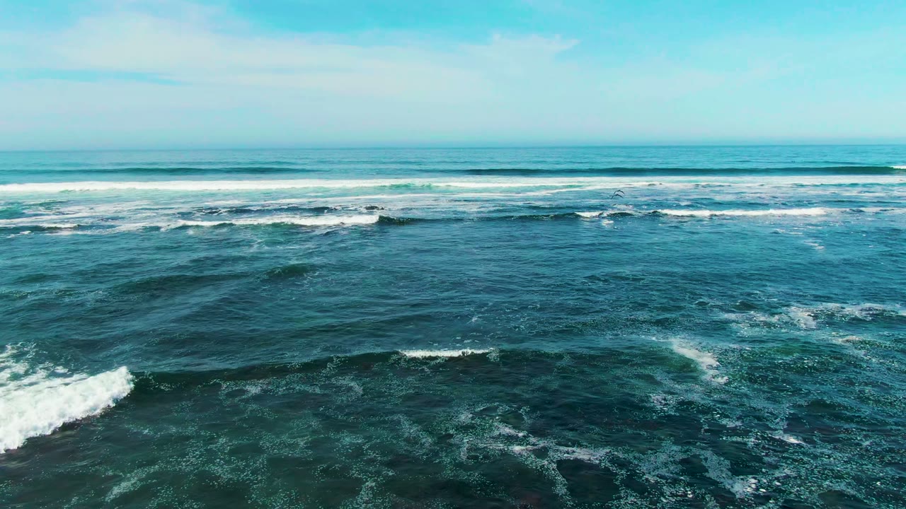 Elevated view of La Bocana surf with a diagonal band of whitewater near center, darker wave texture in the foreground, and no visible people.