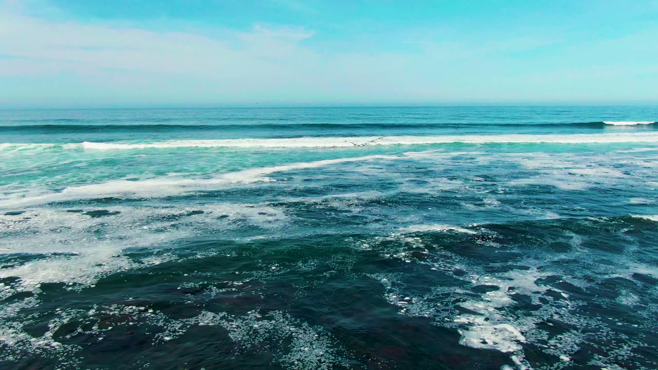 Parallel surf bands break across blue ocean water.