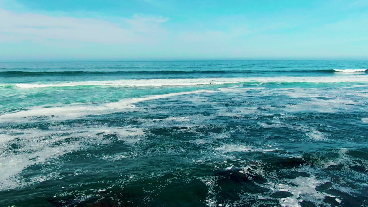 White crests spread across the blue-green sea at La Bocana while the horizon stays level beneath a pale sky, with no visible people.