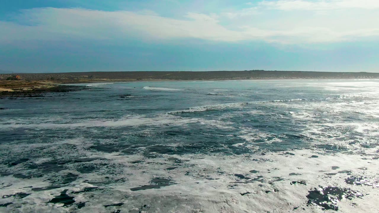 Blue-green ocean with white foam and a low rocky shore at left.