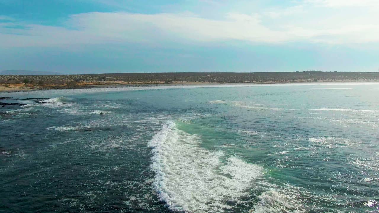 White surf trails across blue-green water toward a low coastal horizon.