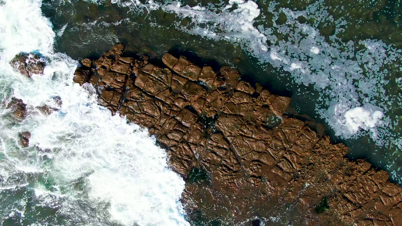 Foam spreading over rocks from an overhead coastal view
