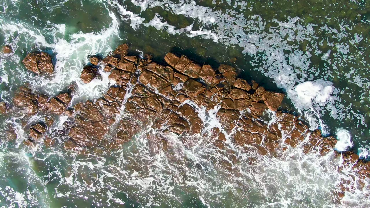 White foam spreads over a rocky ocean outcrop.