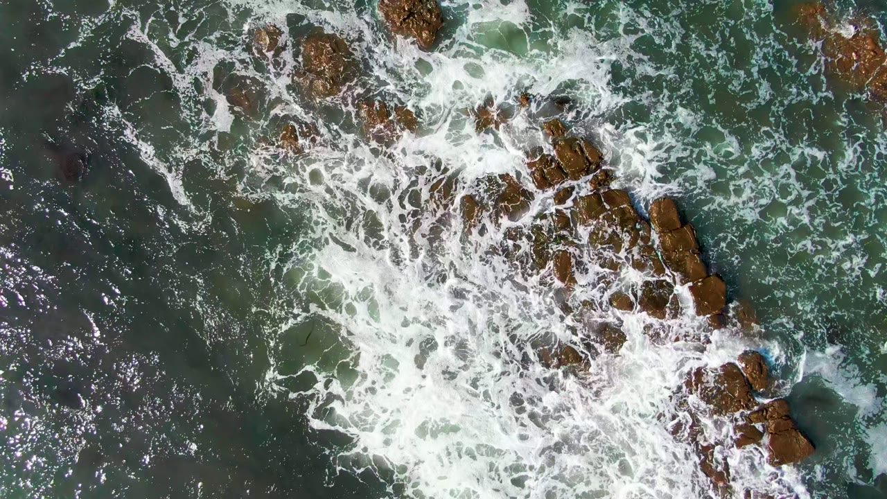 Foamy waves crossing a central rocky outcrop from above