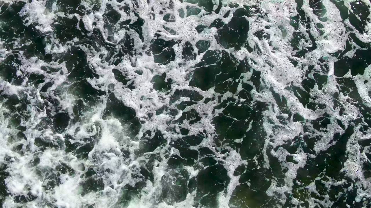 Overhead view from La Bocana showing a busy field of white surf foam over green ocean water, with no visible people or vessels.