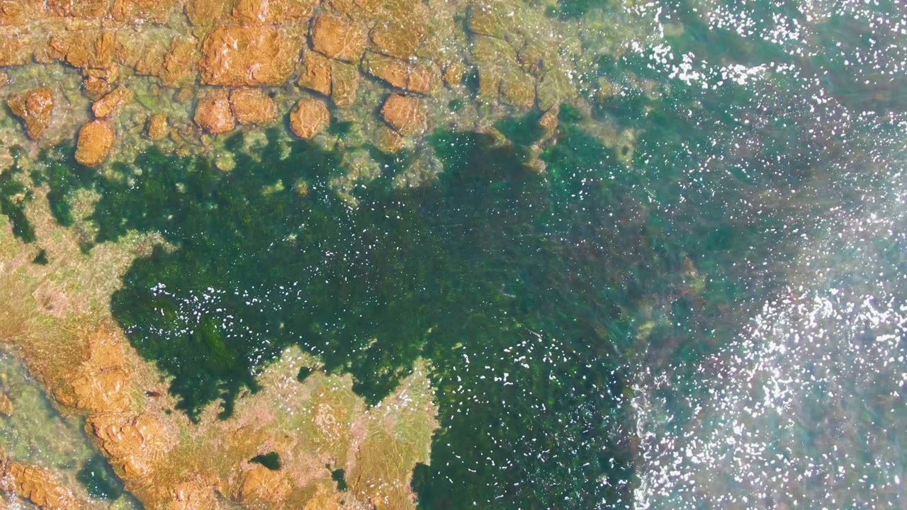 Rock ledges border dark green water with scattered sun reflections.