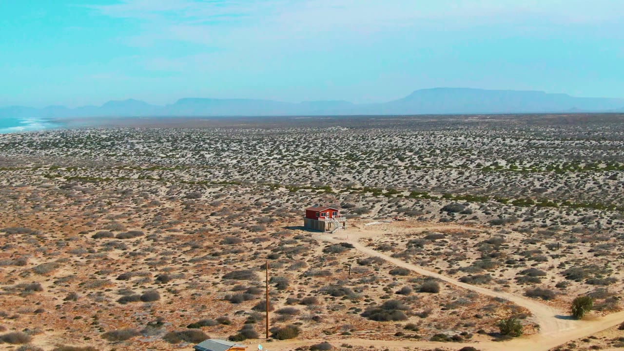 Aerial desert landscape with structure, dirt road, scrub, and mountains.